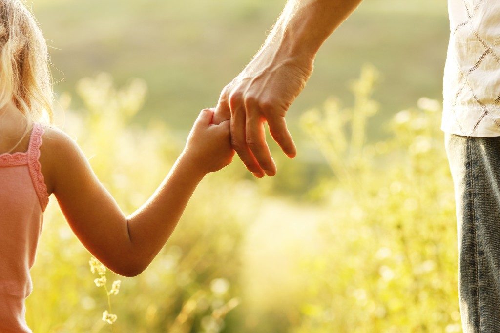 Child holding fathers hand in a garden