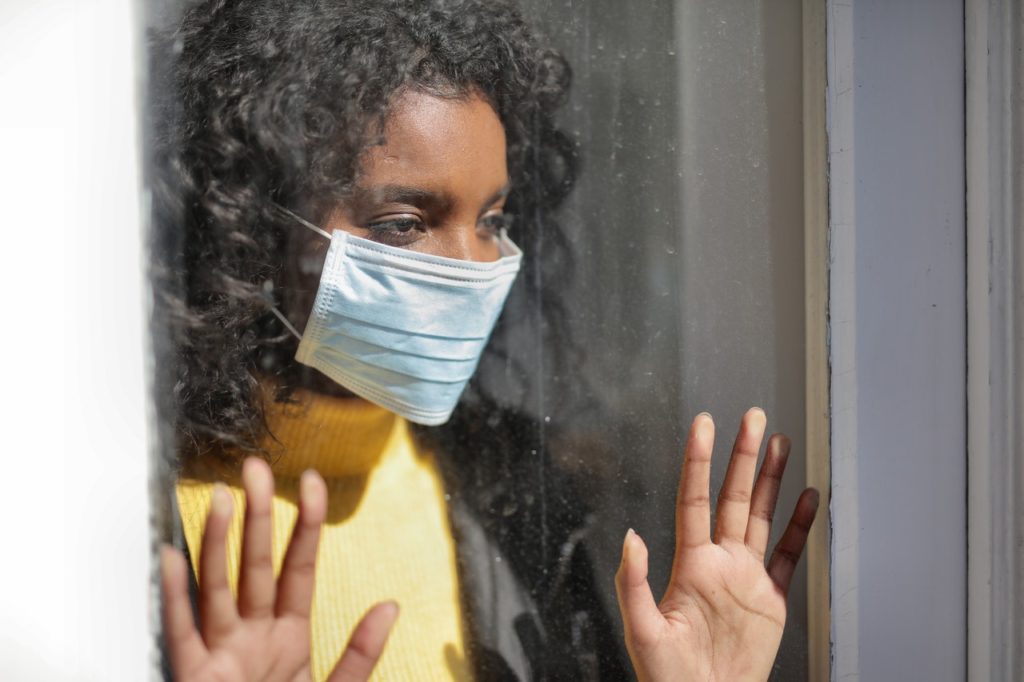 woman wearing facemask staring outside the window